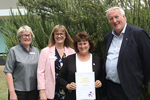 Rockingham Peel Group staff member Eve Grant holds a long service leave certificate while standing with two women and a man outside.