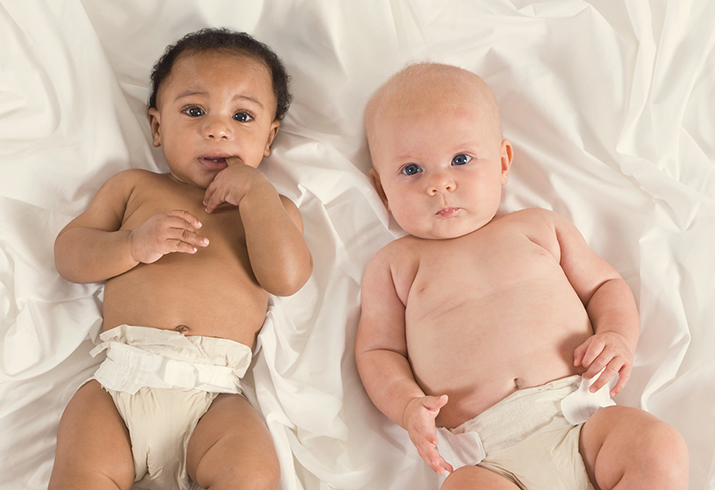 Two babies wearing only a nappy lay side by side