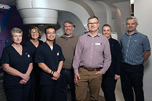 Members of the Rockingham Peel Group Radiation therapy team and ICON Cancer Centre staff stand beside a linear accelerator.