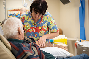 A female nurses reviews a male patient's arm in the chemotherapy unit.
