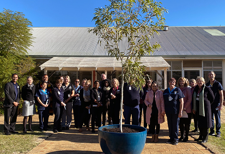 Group of hospital staff stand in front of hospital building.