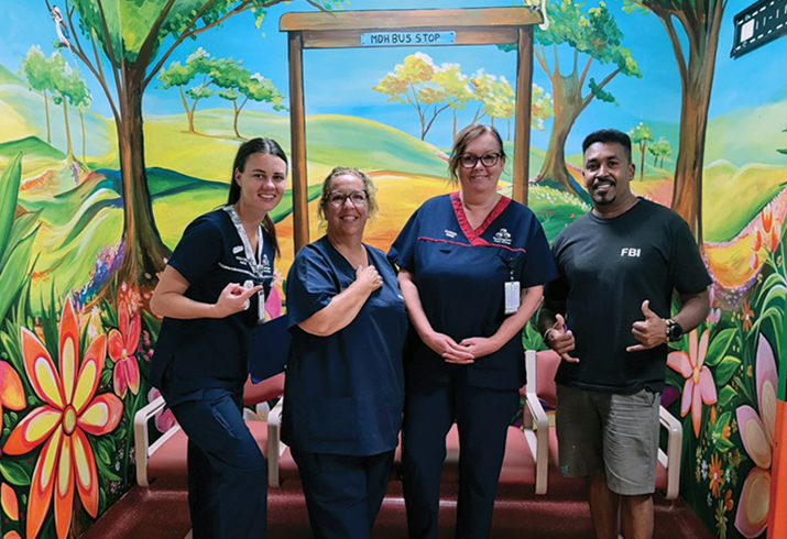 Three Murray District Hospital nurses and a man stand in front of a vivid floral mural 